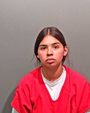 A young individual in a red jail jumpsuit poses for a mugshot against a gray background.