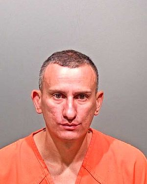 A man in an orange prison jumpsuit stares directly at the camera against a gray background.