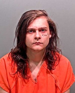 A young individual with long hair and a tattoo reading "DEAD" on their face is shown wearing an orange jumpsuit.