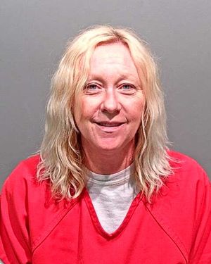 A woman with long, blonde hair is smiling while wearing a red prison jumpsuit against a plain background.