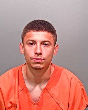 A young man with short hair is shown in a mugshot, wearing an orange prison jumpsuit against a plain gray background.