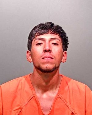 A young man with short black hair is wearing an orange prison jumpsuit and looking directly at the camera.