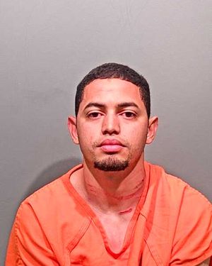 A man wearing an orange jumpsuit poses for a mugshot against a plain gray background.