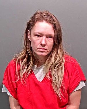 A woman with long, messy hair is wearing a red jail uniform and looking directly at the camera.