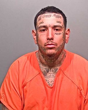 A man with extensive facial tattoos is shown wearing an orange prison jumpsuit.