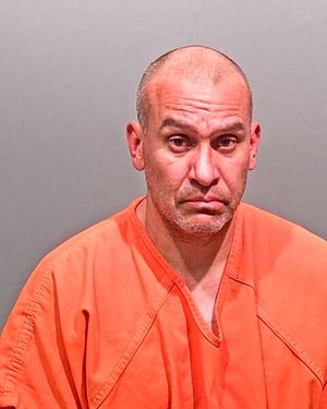 A man wearing an orange prison jumpsuit looks solemnly at the camera.