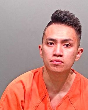 A young man in an orange prison jumpsuit is looking directly at the camera.