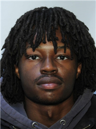 A young man with long, dark dreadlocks wearing a gray hoodie, facing the camera.