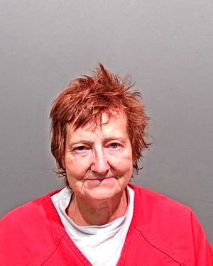 A woman with short, messy reddish-brown hair is wearing a red prison jumpsuit and smiling in a mugshot.