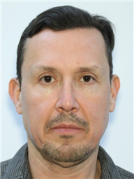 A close-up portrait of a middle-aged man with short dark hair and a light stubble, looking directly at the camera.