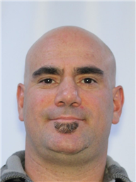 A bald man with a goatee is smiling against a plain background.