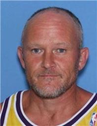 A middle-aged man with a shaved head and beard, wearing a yellow and purple sports jersey.