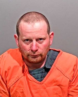 A man dressed in an orange jail uniform is looking directly at the camera.