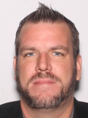 A man with short hair and a beard is looking directly at the camera.