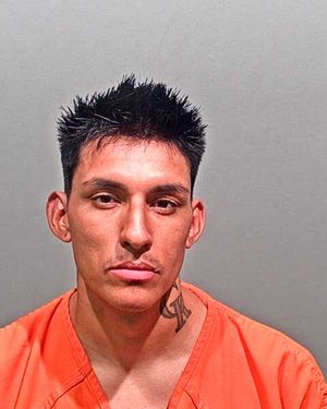 A man with short, spiky hair and a tattoo on his neck is wearing an orange prison uniform and looking directly at the camera.