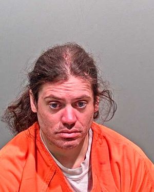 A man with long hair is shown in a mugshot wearing an orange jumpsuit.