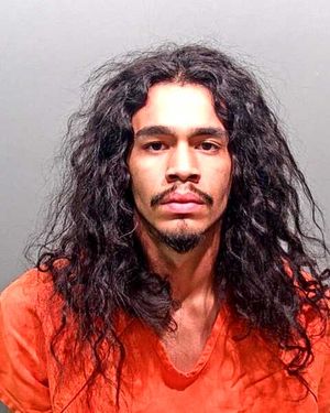 A young man with curly hair is shown wearing an orange prison jumpsuit against a neutral background.