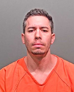 A man wearing an orange jumpsuit is posing for a mugshot against a gray background.
