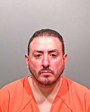 A man wearing an orange jumpsuit is pictured in a mugshot against a gray background.