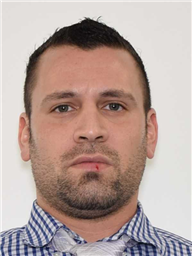 A man with a short beard and a checked shirt poses against a plain white background.