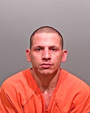 A man in an orange jumpsuit is facing the camera, with a neutral expression and short hair.