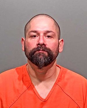 Mugshot of a man with a shaved head and beard, wearing an orange prison jumpsuit.