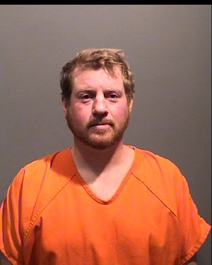 A man is shown wearing an orange prison jumpsuit, looking directly at the camera with a neutral expression.