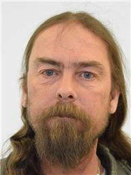 A man with long, unkempt hair and a thick beard is staring directly at the camera against a plain white background.