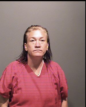 A woman with long hair is posing for a mugshot while wearing a red prison attire.