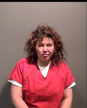 A woman with curly hair is wearing a red prison uniform and is posing for a mugshot against a plain background.