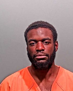 A man with a beard is wearing an orange prison jumpsuit and staring directly at the camera.