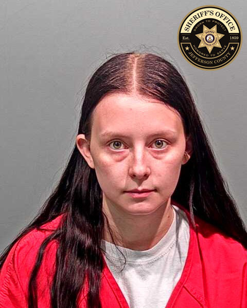 White famale with long brown hair, wearing a red jail jumpsuit