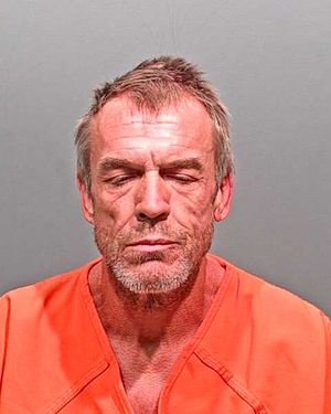 A man with disheveled hair and a rugged appearance is shown in an orange prison jumpsuit, facing the camera with a solemn expression.