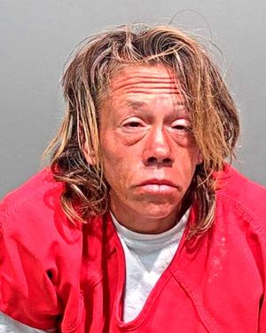 A person with long, tousled hair wearing a red prison jumpsuit appears in a mugshot.