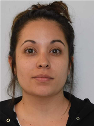 A woman with dark hair pulled back and a neutral expression is shown against a plain background.