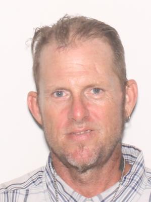 A middle-aged man with short hair and a beard is smiling in front of a plain white background.