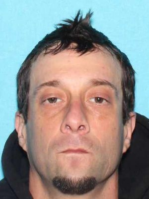 The image shows a close-up headshot of a man with short, spiked hair and a goatee, wearing a black hoodie.