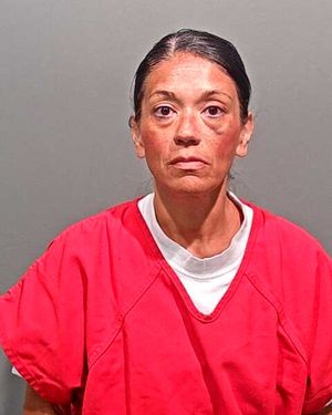 A woman wearing a red prison jumpsuit is posing for a mugshot against a gray background.