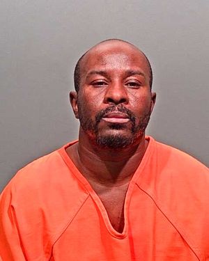 A man in an orange jumpsuit is shown posing for a mugshot against a gray background.