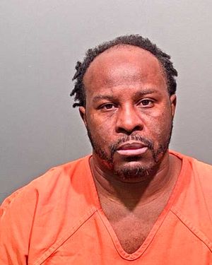 A man wearing an orange prison jumpsuit is posing for a mugshot against a plain background.