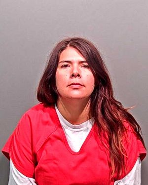 A woman with long, dark hair is shown facing forward while wearing a red prison jumpsuit against a gray background.