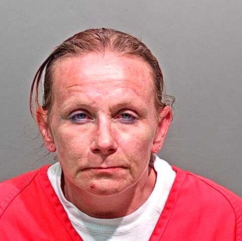 Jolene looking at the camera in an bright red jail jumper on a grey background with hair slicked back. 