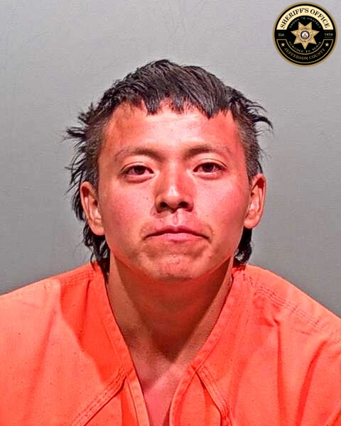 Royce staring at camera with frown, wearing orange jump suit and messy brown hair. 